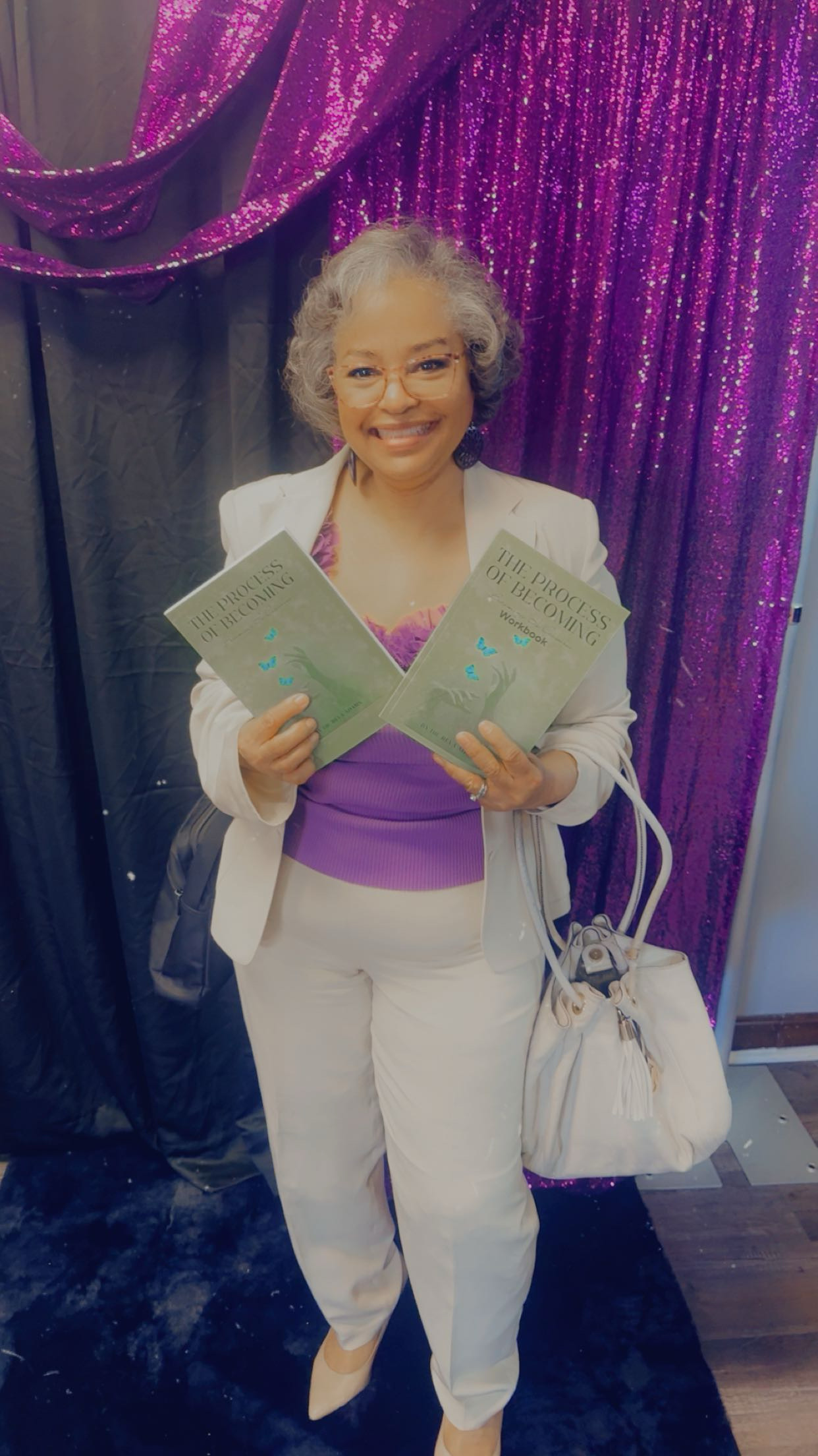 Woman in white blazer proudly holding The Process of Becoming books